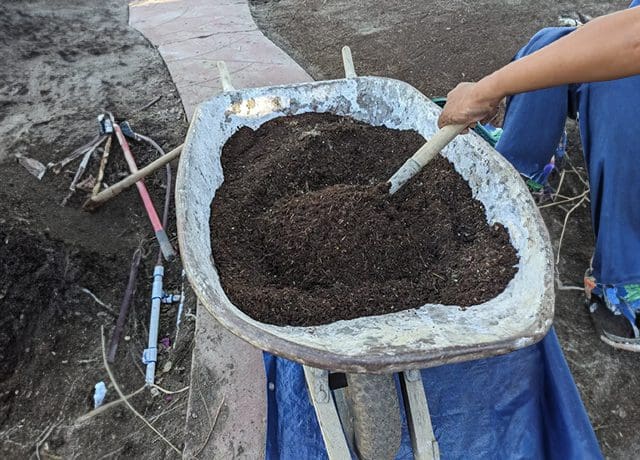 A person is holding a wheelbarrow full of dirt.