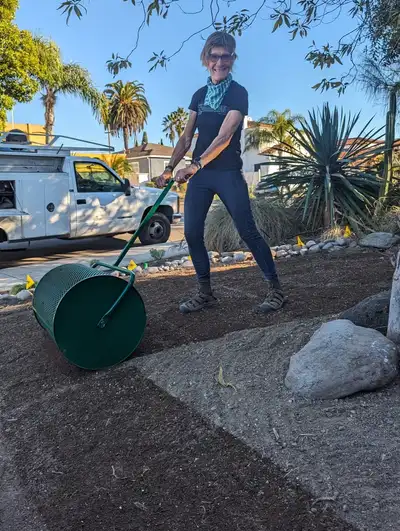 A woman is rolling a barrel of dirt.