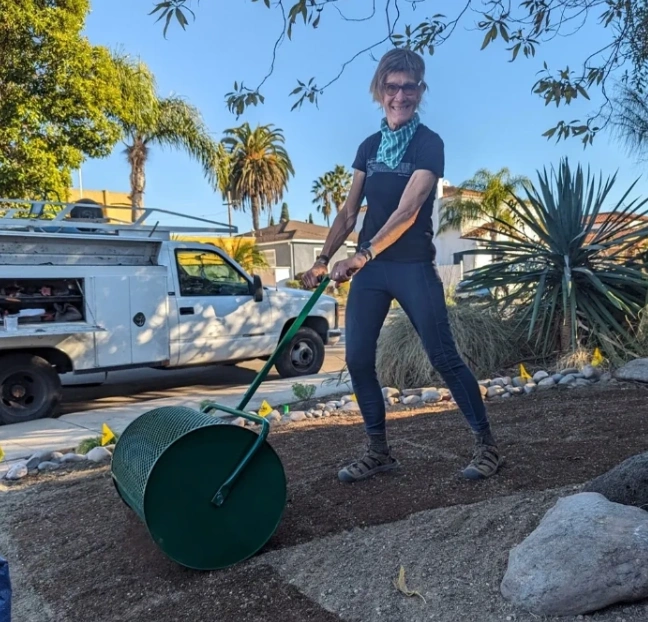 A woman is using a lawn roller to spread the dirt.