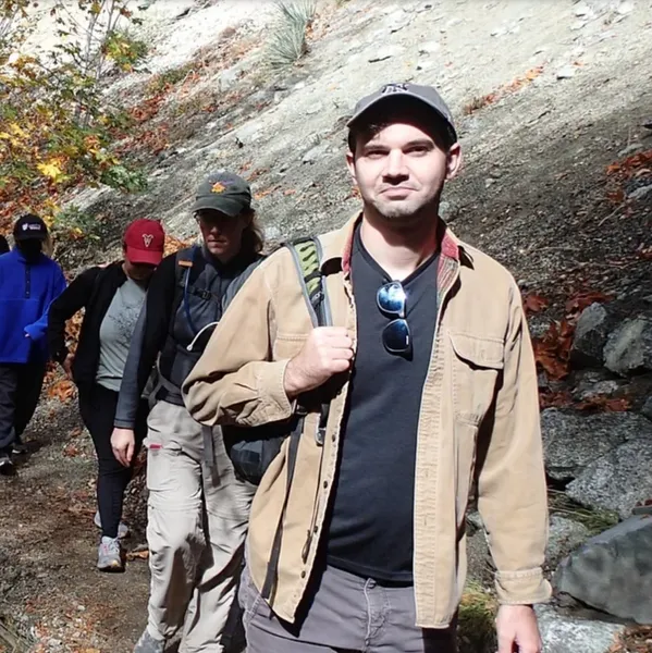 A man in brown jacket and hat walking on trail.