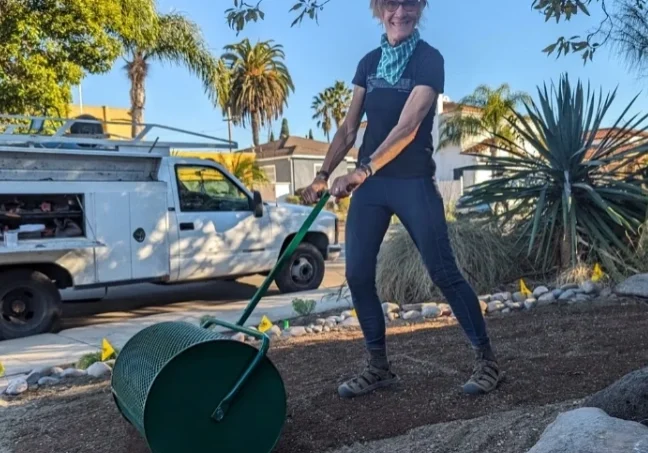 A woman is using a lawn roller to spread the dirt.